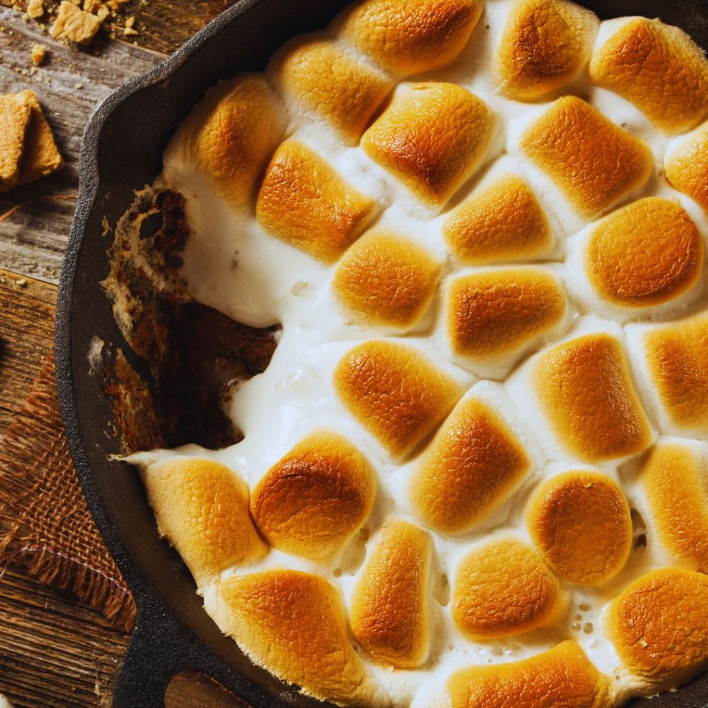 a cast iron skillet of brown toasted marshmallows with a bite missing and chocolate underneath