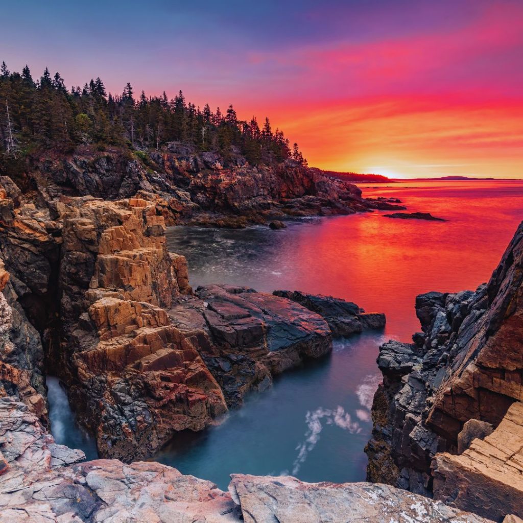 Acadia national park cliffs at sunset with the water below and a pink and orange reflection of the sky