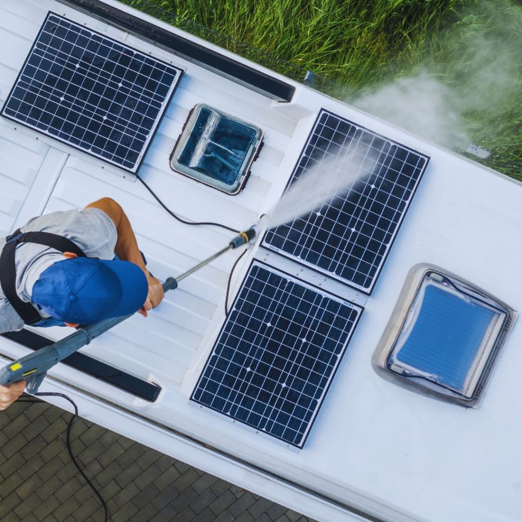 man with a blue hat cleaning the solar panels on the top of an RV