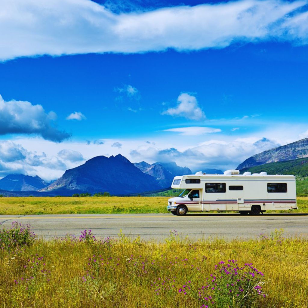 Motorhome parked on the side of the road between fields of grass and wildflowers with blue mountains in the distance